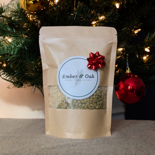 Pouch of Ember & Oak product with a red bow in front of a decorated Christmas tree.